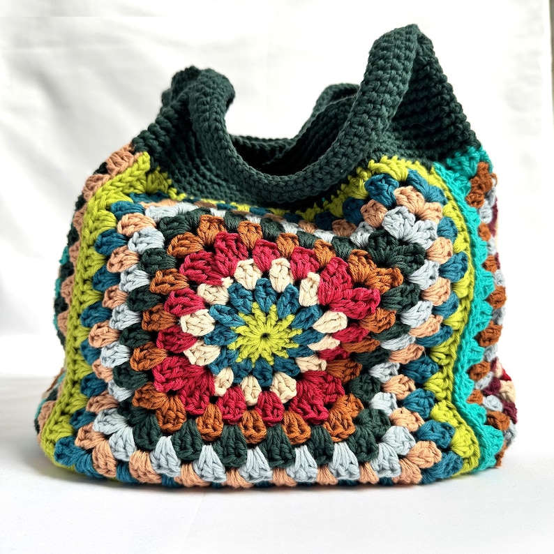 Puede incluir: Bolso tote de crochet hecho a mano con un dise&ntilde;o de cuadrados de la abuela colorido. El bolso presenta un asa y ribete verde oscuro, con una vibrante mezcla de cuadrados rojos, amarillos, azules y marrones. Un accesorio elegante y funcional.
