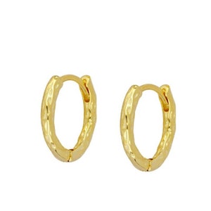 May include: A pair of gold-toned hoop earrings with a hammered texture. The earrings are small and delicate.