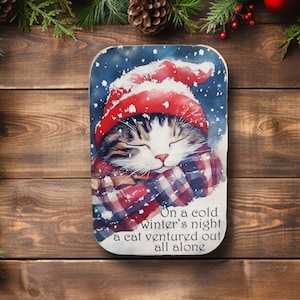 May include: A rectangular decorative item featuring a watercolor painting of a sleeping cat wearing a red hat and plaid scarf. The text reads, "On a cold winter's night a cat ventured out all alone."