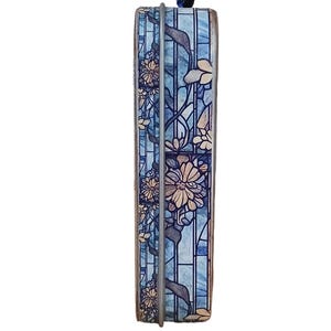 Puede incluir: Una caja decorativa rectangular con un dise&ntilde;o floral. La caja presenta un efecto de vidriera azul con flores beige y hojas verdes. Un marco de metal plateado rodea la caja, y un peque&ntilde;o elemento decorativo azul oscuro se encuentra en la parte superior.