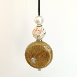 Peut inclure: Un cordon de tirage décoratif composé d'une grande perle en céramique brun olive brillant à la base, surmontée d'une perle en céramique blanche et rose mouchetée, d'une perle blanche nacrée et d'entretoises argentées sur un cordon noir.