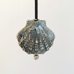 May include: A ceramic seashell light pull with a black cord. The seashell is gray and white with a textured surface.