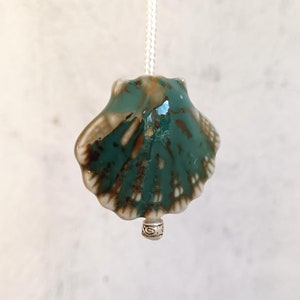 May include: A ceramic light pull shaped like a seashell with a teal and brown glaze. The pull has a silver metal ring at the bottom.