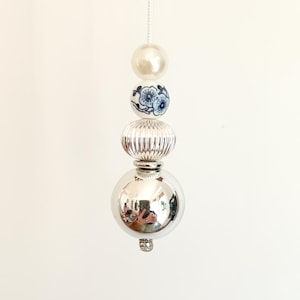 May include: A light pull cord featuring a vertical arrangement of beads. The sequence includes a smooth cream bead, a white ceramic bead with blue floral patterns, a ribbed silver-tone bead, and a large, reflective chrome-finished sphere.
