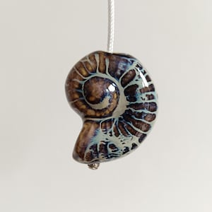 May include: A ceramic light pull shaped like a nautilus shell with brown, blue and white swirling patterns.