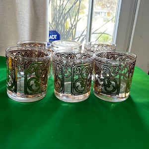 May include: Set of six clear glass tumblers with gold and green geometric designs. The glasses have a vintage look and are perfect for serving drinks.