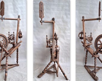 May include: A brown wooden spinning wheel featuring a large circular wheel, a treadle base, and a vertical distaff. The frame is constructed with turned legs and includes a flyer mechanism with a bobbin. The wood has a dark finish.