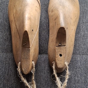 May include: Two wooden shoe lasts with a brown finish and a rope tied to the bottom of each. The lasts are used for shaping shoes.