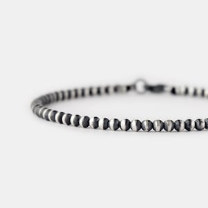 Op de afbeelding: Een zilveren kralen armband met een donker geoxideerde afwerking. De armband is gemaakt van kleine, ronde kralen die gelijkmatig zijn verdeeld.