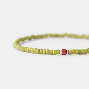 May include: A delicate green beaded bracelet with a single red bead accent.