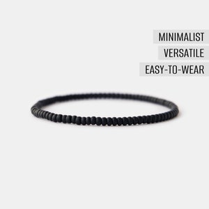 May include: A black beaded bracelet with a minimalist design. The bracelet is made of small, round beads that are strung together on a thin cord.