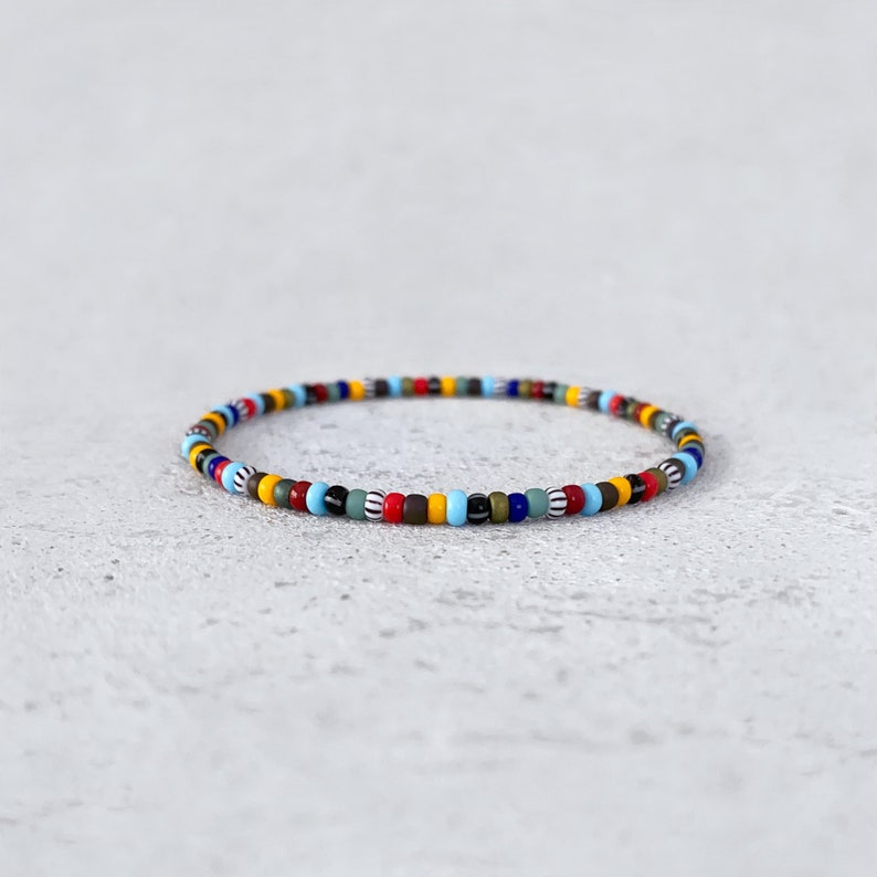 May include: A colorful beaded bracelet with a mix of red, blue, yellow, green, black, and white beads.