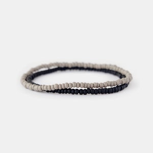May include: A simple bracelet made of two strands of small beads. One strand is black and the other is a light gray.