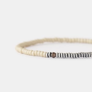 May include: A white and silver beaded bracelet with a brown gemstone accent.