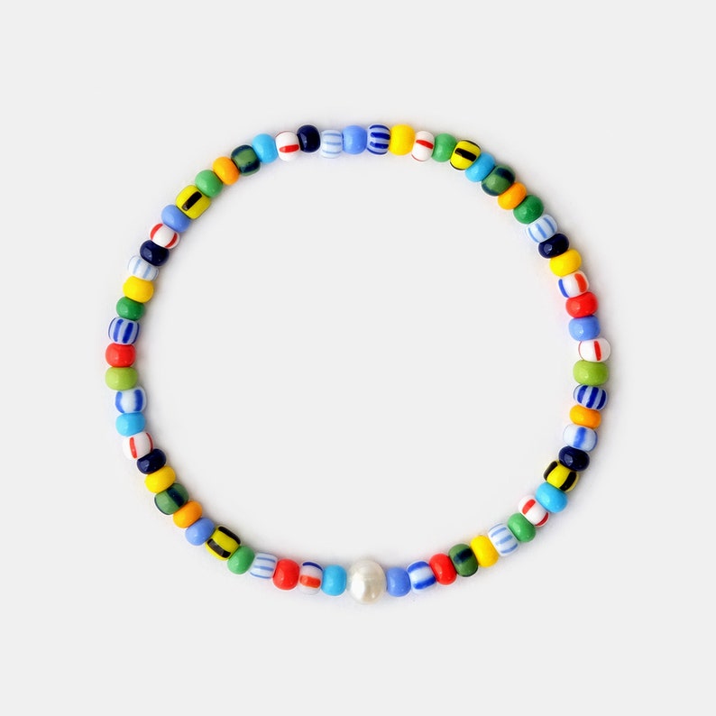 May include: A colorful beaded bracelet with a pearl charm. The beads are in various colors, including blue, green, yellow, red, and white.