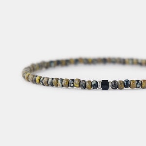Könnte beinhalten: Ein Armband mit schwarzen und braunen gesprenkelten Perlen und einer einzelnen schwarzen Perle als Akzent.