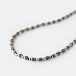 May include: A silver and green beaded necklace with small, square-shaped beads.