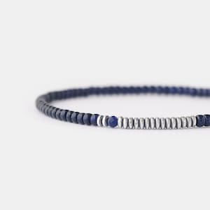 Könnte beinhalten: Ein blaues und silbernes Perlenarmband mit einer einzigen größeren blauen Perle in der Mitte.