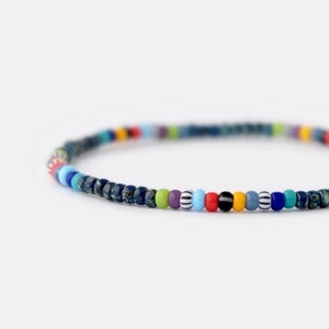 May include: A colorful beaded bracelet with a mix of blue, green, purple, red, yellow, and white beads. The bracelet is made with small, round beads.