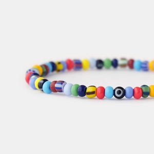 May include: A colourful beaded bracelet with a variety of colours, including blue, green, red, yellow, and black. The bracelet features a single evil eye bead.