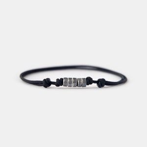 May include: A black cord bracelet with a row of silver beads.