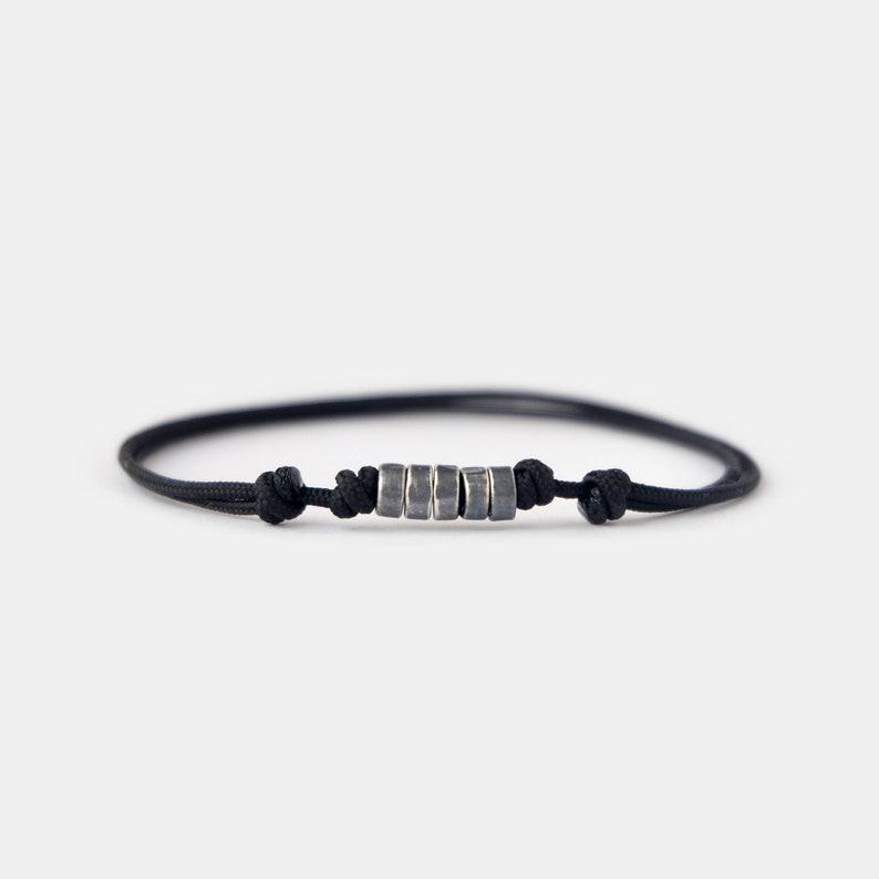May include: A black cord bracelet with a row of silver beads.