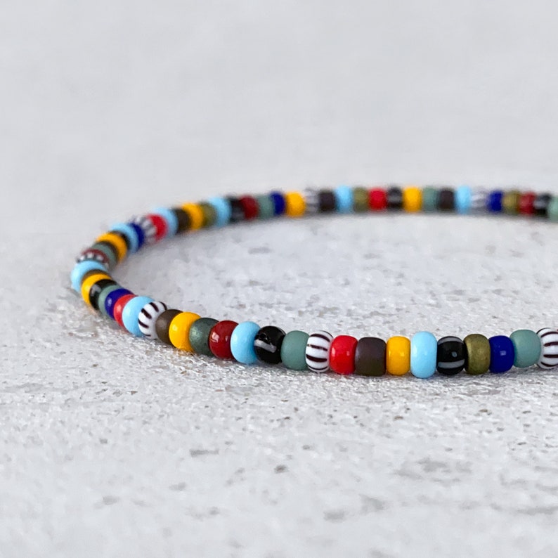 May include: A colorful beaded bracelet with a mix of red, yellow, blue, green, black, and white beads.