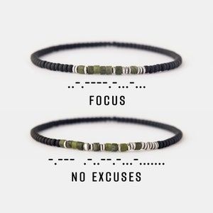Può includere: Due braccialetti neri con perline verdi e argentate che compongono le parole "FOCUS" e "NO EXCUSES" in codice Morse.