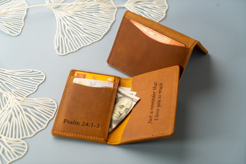Może przedstawiać: Dwa brązowe sk&oacute;rzane portfele z spersonalizowanym napisem. Jeden portfel ma napis "Psalm 24:1-3", a drugi "Tylko przypomnienie, że bardzo cię kocham".