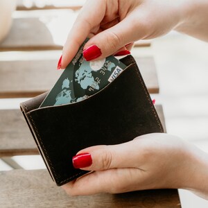 Może przedstawiać: Brązowy sk&oacute;rzany portfel, z kt&oacute;rego wyciągana jest karta kredytowa. Karta ma wz&oacute;r mapy świata i napis "VISA" nadrukowany na niej.
