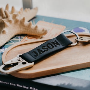 May include: A black leather keychain with a silver clip and a key ring. The keychain has the name "JASON" engraved on it.