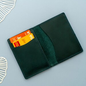 Może przedstawiać: Portfel sk&oacute;rzany w ciemnozielonym kolorze z dwoma kartami kredytowymi w środku. Karty są pomarańczowe i ż&oacute;łte z nadrukiem "VISA".