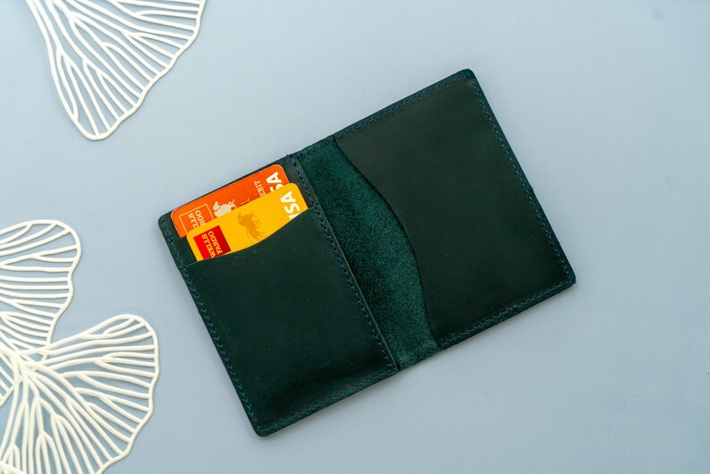 Może przedstawiać: Portfel sk&oacute;rzany w ciemnozielonym kolorze z dwoma kartami kredytowymi w środku. Karty są pomarańczowe i ż&oacute;łte z nadrukiem "VISA".
