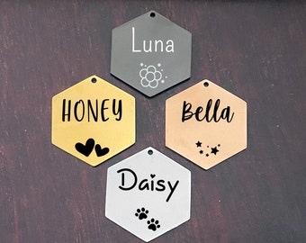 May include: Four hexagonal pet ID tags with different names and designs. The tags are made of metal and have a silver, gold, and bronze finish. The names on the tags are "Luna", "Honey", "Bella", and "Daisy".