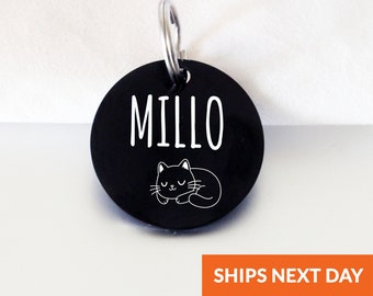 以下が含まれることがあります： 白い寝ている猫のデザインと白い文字で「MILLO」という名前が書かれた黒い丸いペット用IDタグです。