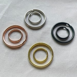 May include: Four different key rings, each with a different color and size. The key rings are made of metal and have a circular shape. The key rings are arranged in a circle on a white surface.