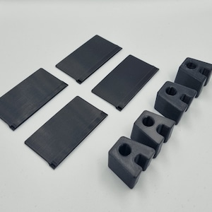 Puede incluir: Cinco soportes de estantería de plástico negro y cuatro soportes de estantería de plástico negro. Los soportes de estantería son rectangulares y los soportes de estantería tienen forma de letra 'L'.