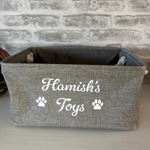 May include: A gray fabric storage bin with the text "Hamish's Toys" and two white paw prints embroidered on the front.