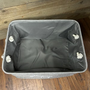 May include: A gray fabric storage bin with white rope handles. The bin has a gray liner and the words "Live Simply" are printed on the front.