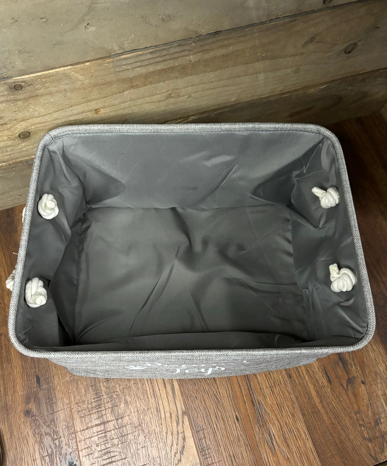 May include: A gray fabric storage bin with white rope handles. The bin has a gray liner and the words "Live Simply" are printed on the front.