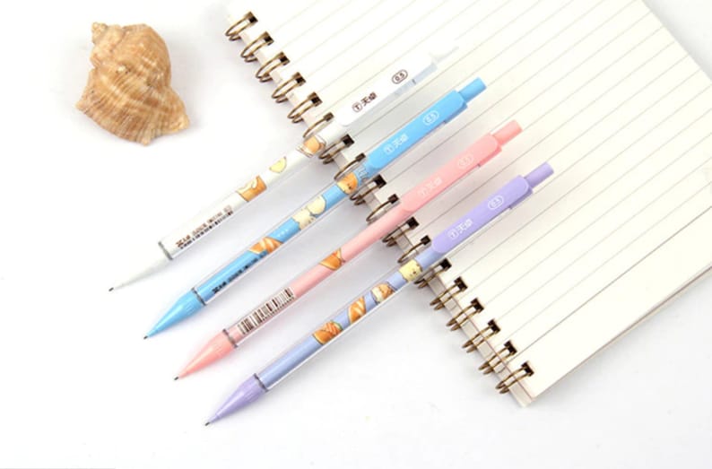 May include: Five colorful mechanical pencils with a white background. The pencils have a clear barrel with a cute cartoon design and a colored tip. The pencils are arranged in a row, with the tips pointing to the right.