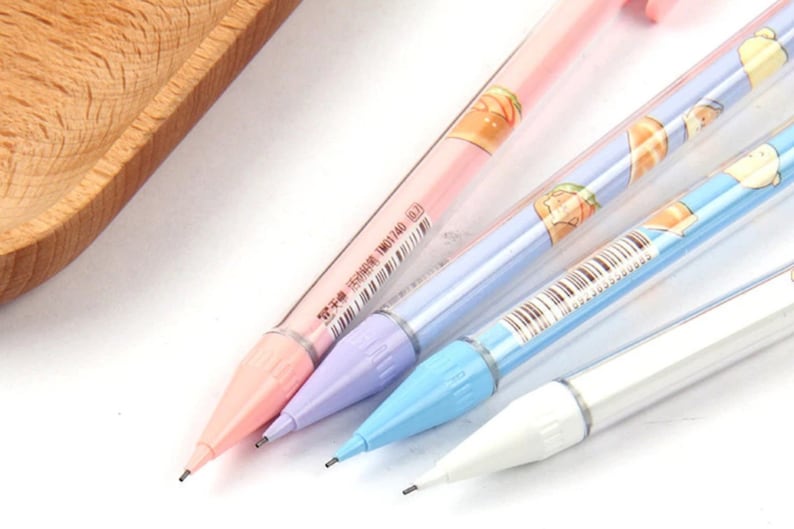 May include: Four colorful mechanical pencils with cartoon characters and text on the barrels. The pencils are pink, light blue, purple, and white.