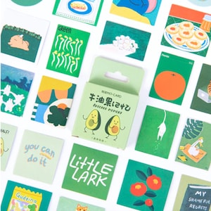 Könnte beinhalten: Ein Set mit 30 grünen und weißen Aufklebern mit verschiedenen Illustrationen, darunter Avocados, Orangen, Katzen und Pflanzen. Die Aufkleber sind in einer kleinen grünen Box verpackt, auf der "牛油果记忆 Avocado Memory" in Japanisch und Englisch steht.