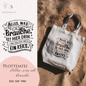 May include: A white tote bag with black text that reads "Alles, was ich brauche, ist hier drin... und vielleicht noch ein Keks." The bag is lying on a sandy surface.
