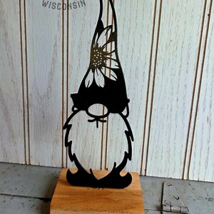 May include: Black metal gnome silhouette with a sunflower design on the hat, mounted on a small wooden base. The gnome has a long beard and a pointed hat. The text "TIN & TIMBER WISCONSIN" is visible in the background.