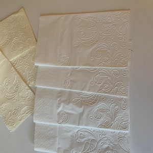 May include: A stack of five white paper napkins with an embossed floral design. The napkins have a delicate, intricate pattern of leaves and swirls.
