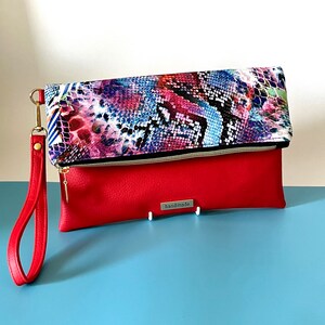 May include: A red and blue patterned clutch with a red flap and a gold zipper. The clutch has a gold chain strap and a "handmade" tag.