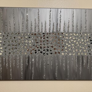 May include: A silver and grey abstract painting with a textured glitter finish. The painting features a horizontal band of small, mirrored squares in the centre, surrounded by vertical lines of glitter.