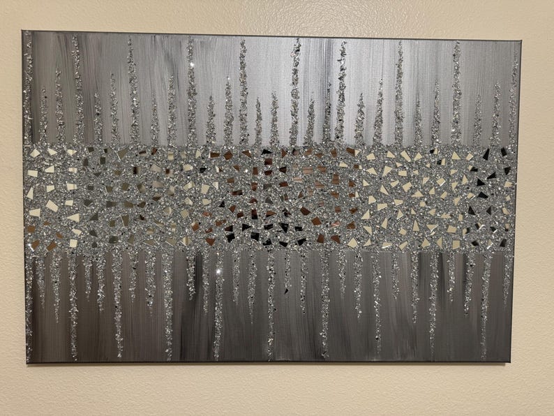 May include: A silver and grey abstract painting with a textured glitter finish. The painting features a horizontal band of small, mirrored squares in the centre, surrounded by vertical lines of glitter.