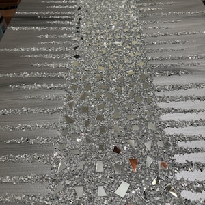 May include: A grey canvas wall art featuring a vertical design of silver glitter and small mirrored pieces. The glitter and mirrored pieces are arranged in a cascading pattern.